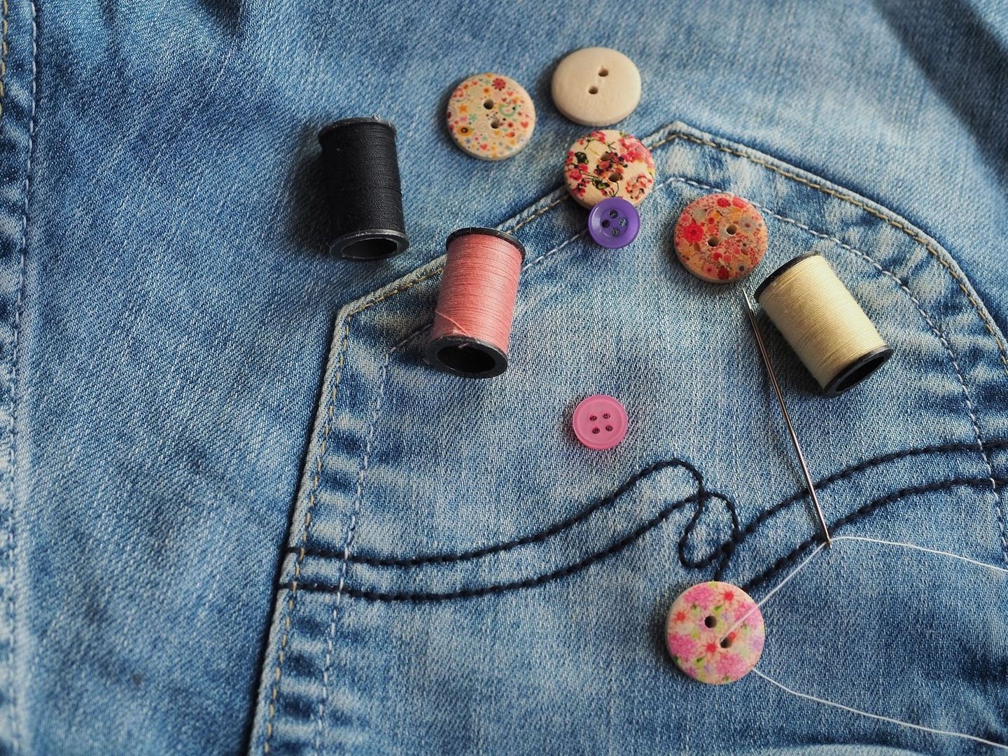 Färgglada sytrådar, knappar och nål på ett par jeans