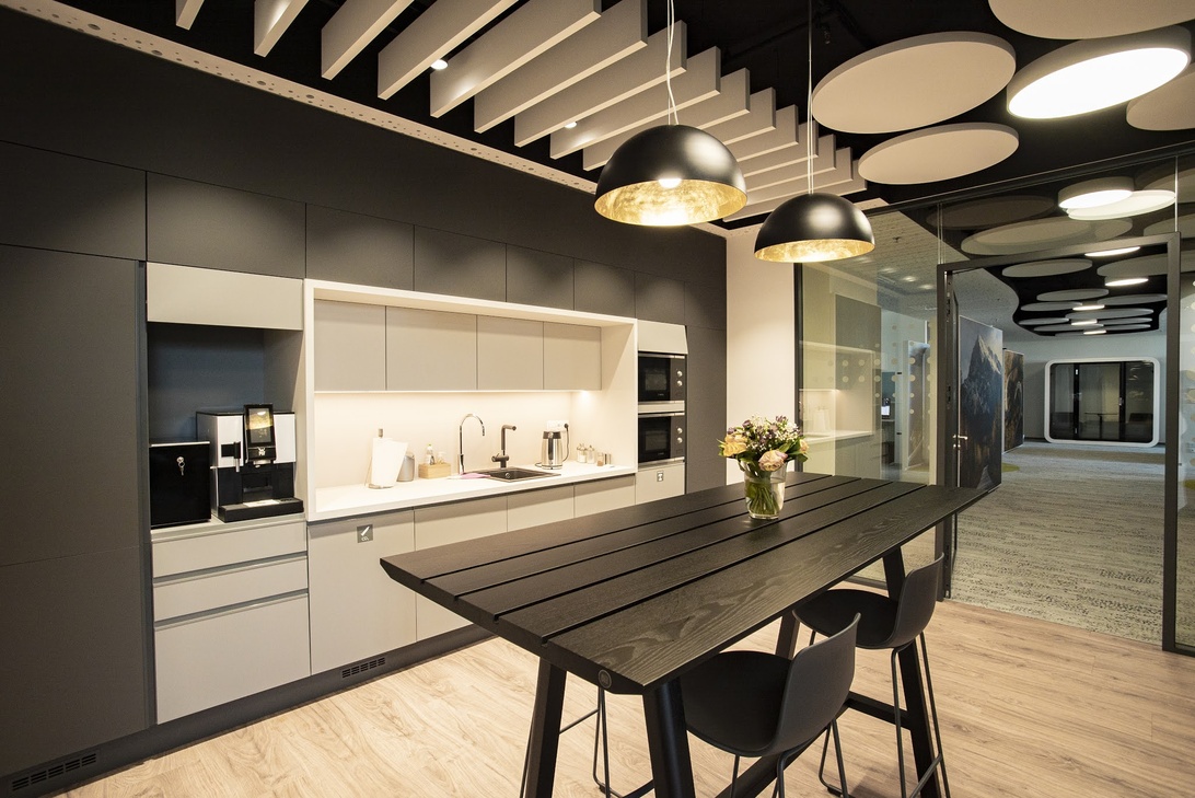 Ett stilrent och modernt kök/pausutrymme på ett kontor, med minimalistisk inredning och designbelysning.